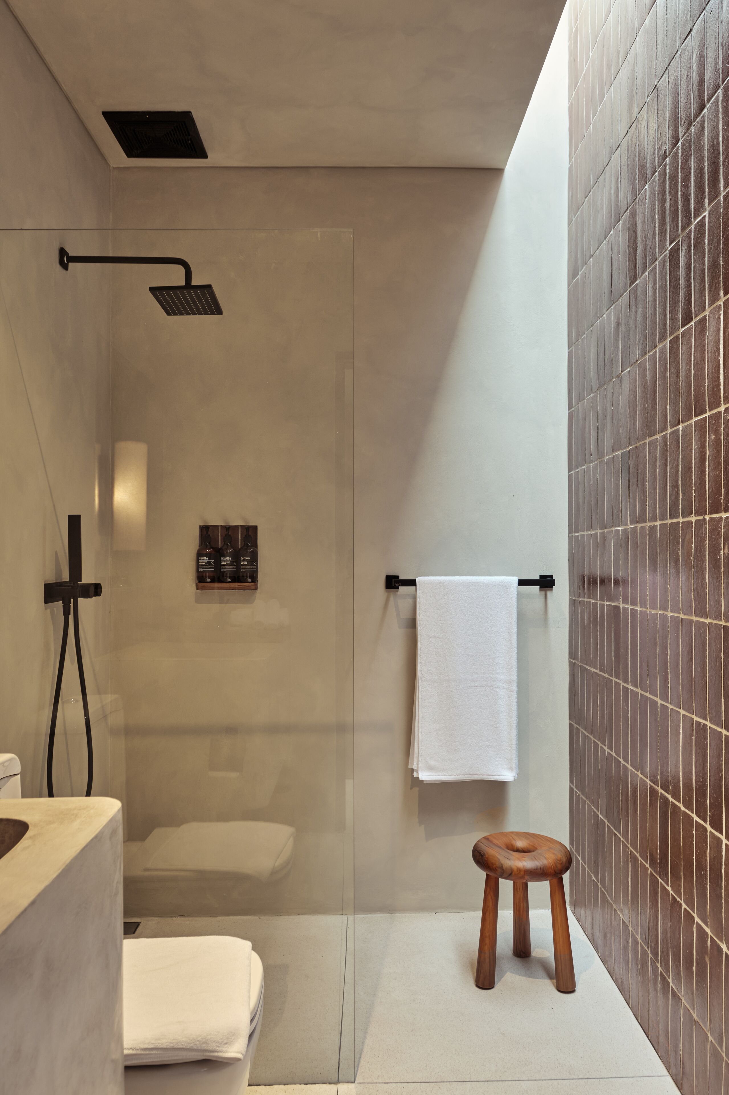 Ein modernes Badezimmer mit einer gläsernen Duschkabine, einem hölzernen Hocker und einem Handtuchhalter.