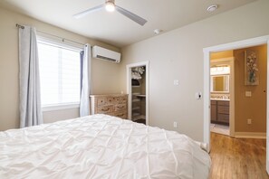 A bedroom with a bed, a ceiling fan, an air conditioning unit, a wardrobe, and a bathroom visible through an open door. - Modern Home with Private Firepit (Coeur d'Alene)
