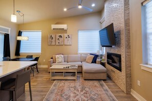 A living room with a sofa, coffee table, and TV mounted on a stone wall. - Modern Home with Private Firepit (Coeur d'Alene)