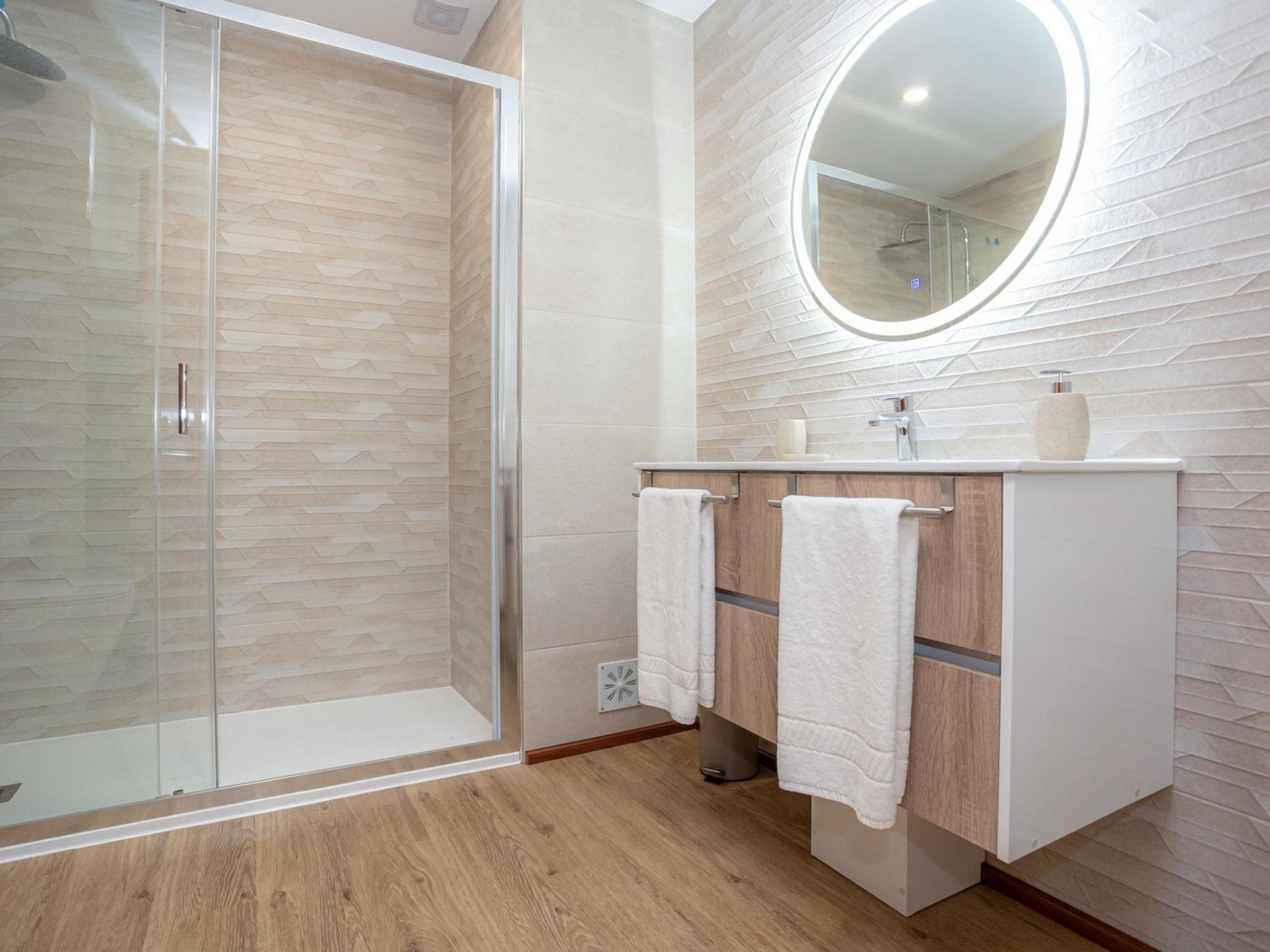 Un baño moderno con cabina de ducha de vidrio, tocador de madera con espejo y pared revestida de azulejos.