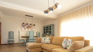 A living room with a beige sectional sofa, two matching armchairs, a wooden coffee table, and a dining area with a table and chairs.