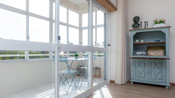 A balcony with a glass door, a small table with chairs, and a decorative cabinet with shelves.