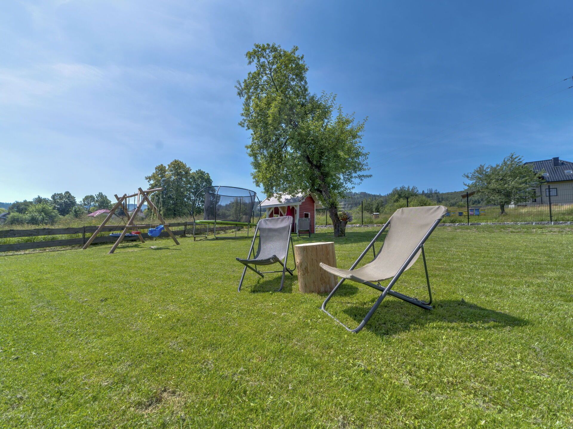 Un espace extérieur comprenant une pelouse, une balançoire, un trampoline et deux chaises longues.