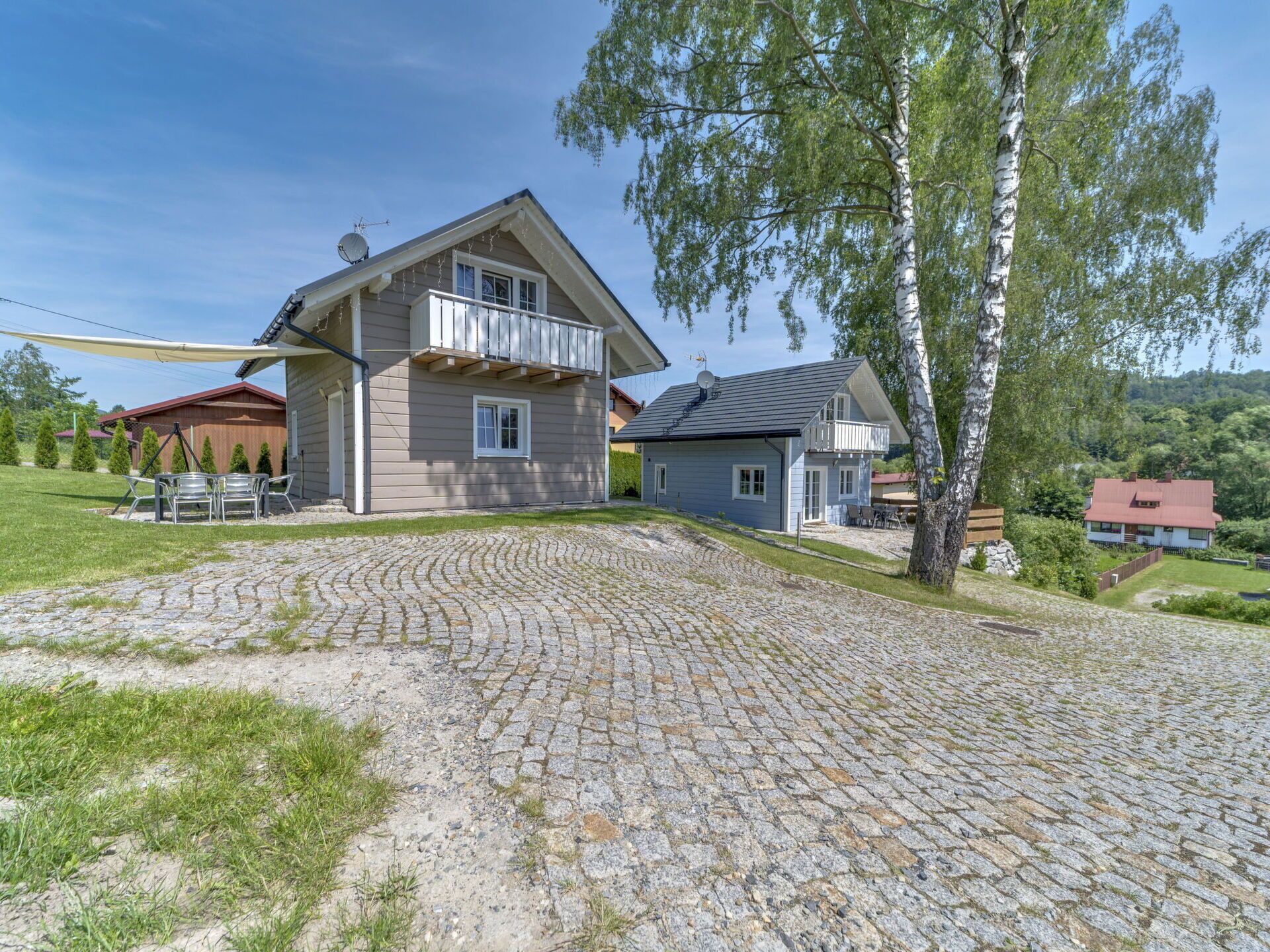 Une maison à deux étages avec une allée pavée de pierres, un balcon et une vue sur le paysage environnant.