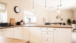 A kitchen with white cabinetry, a wooden countertop, pendant lights, a clock, and a window with a view. - The Barn in Longhope - Luxury Barn Conversion (Longhope)