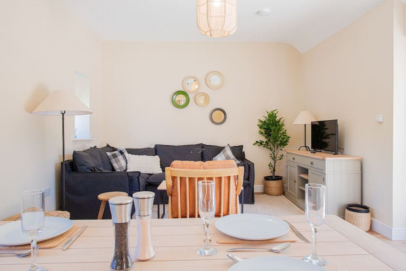 Ein modernes Wohnzimmer mit einem dunklen Sofa, einem Holzespeisetisch für zwei Personen und einem Fernseher auf einer Kommode.