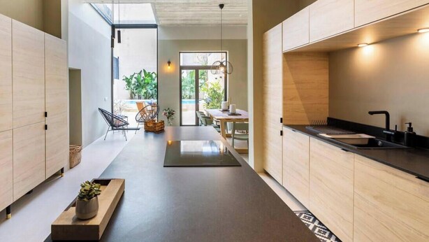A modern kitchen with wooden cabinets, a black countertop, and a sink. There is a dining area with a table and chairs, and a view of the outdoors. - Ultimate luxury home experience in beautiful Rabat (Ir-Rabat)