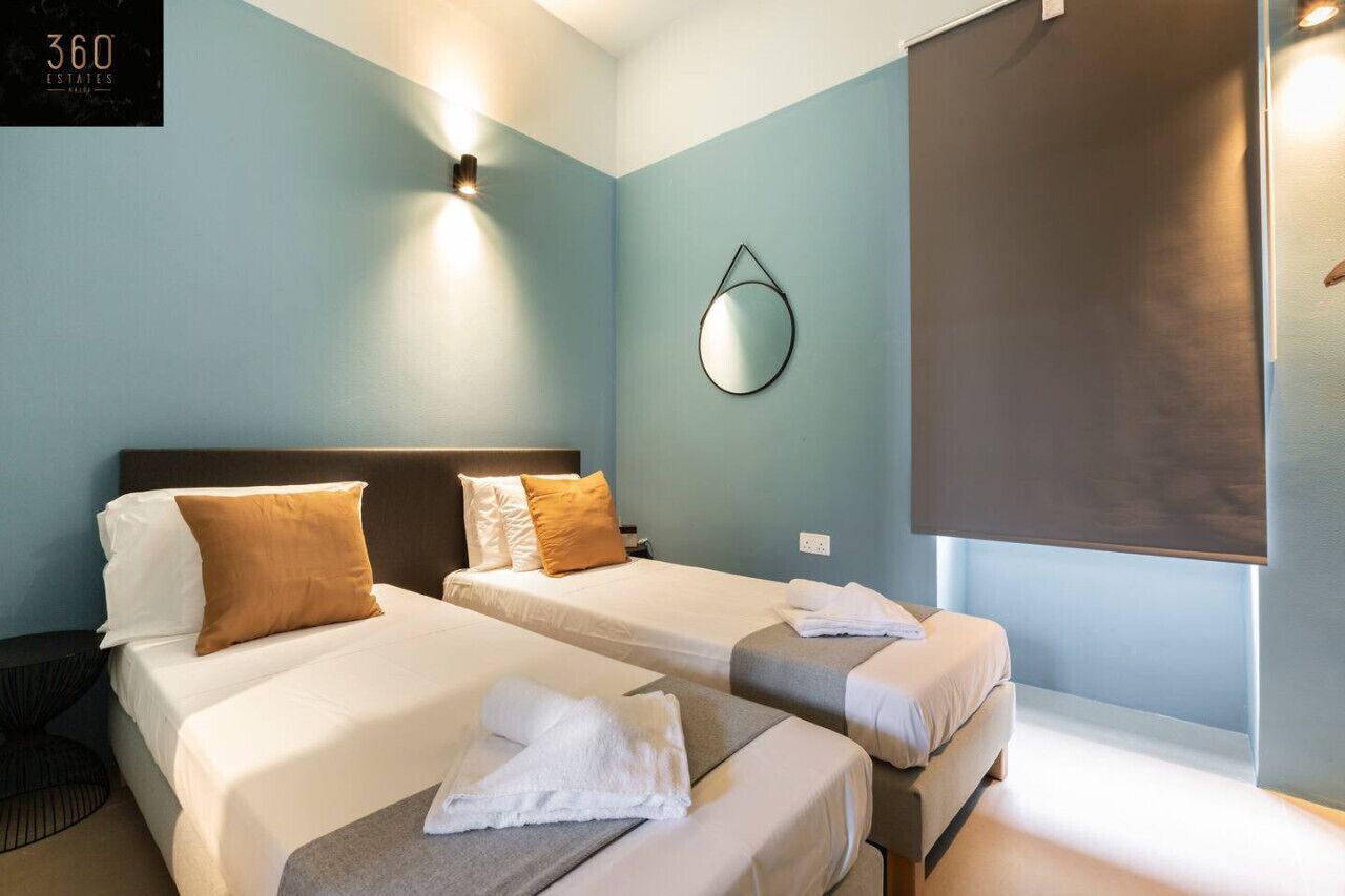 A hotel room with two beds, a wall-mounted mirror, and a large window with a blind.
