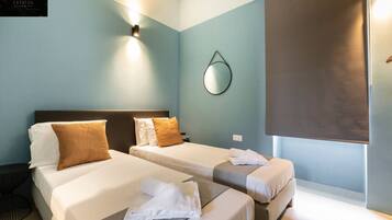 A hotel room with two beds, a wall-mounted mirror, and a large window with a blind.