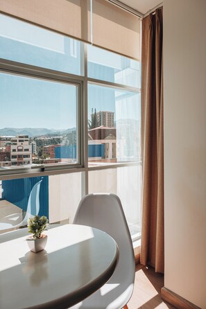 A modern hotel room with a large window, a round table, a potted plant, and a view of the cityscape. - Fratelli Corp Apart Hotel (La Paz)