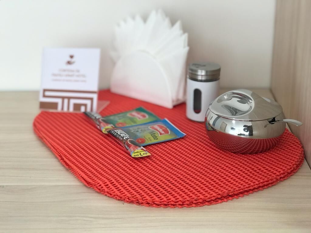 Un tapete rojo con una tetera, una termo, una tarjeta y un pequeño paquete sobre una superficie de madera.