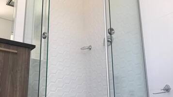 Cabina de ducha con paredes de azulejos hexagonales y cerramiento de vidrio.