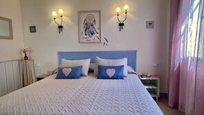 Une chambre à coucher avec un lit, deux lampes fixées au mur, un attrape-rêves et une table de chevet avec une télécommande.