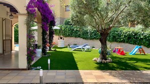 Un jardin bien entretenu, avec une pelouse, un arbre et des jeux pour enfants.