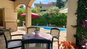 Une terrasse avec une table et des chaises, une piscine et une vue sur un immeuble doté d’un balcon.