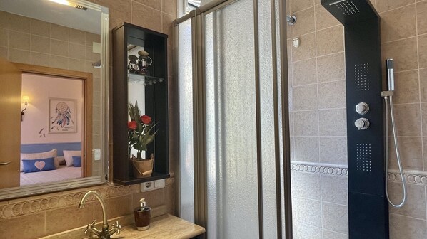 A bathroom with a shower, a sink, a mirror, and a vase with flowers. - VILLA PINEDA 5 (Pals)