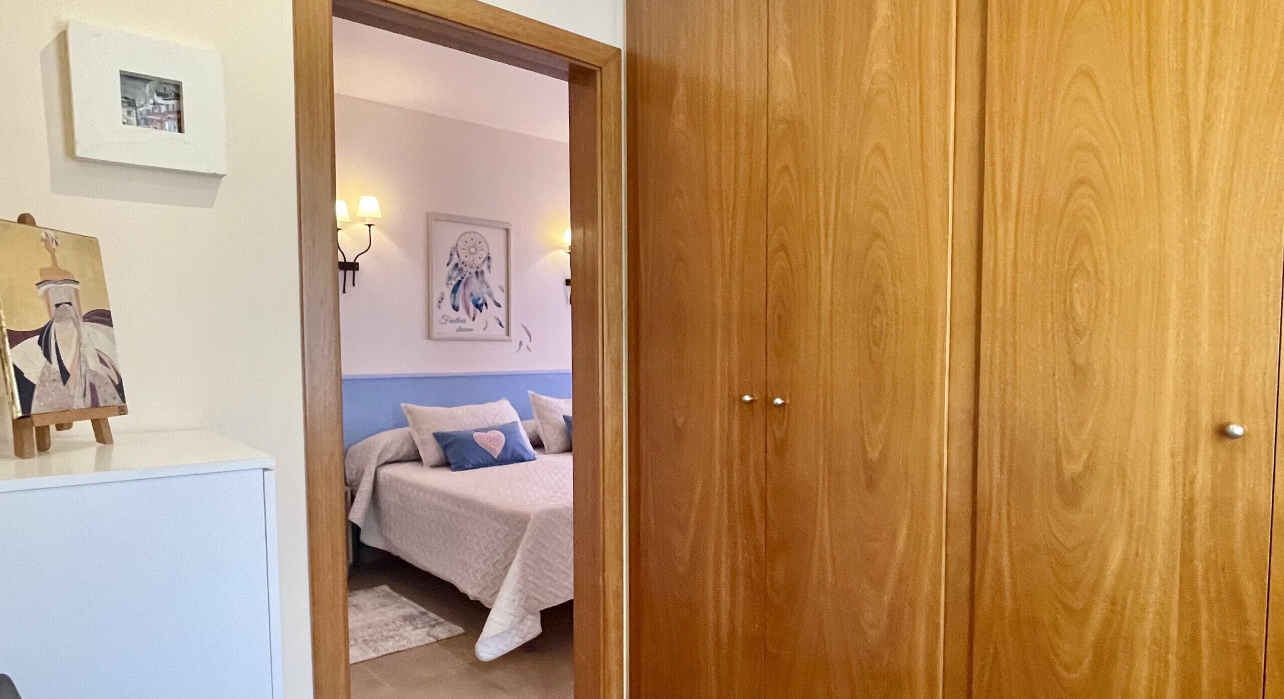 Une chambre à coucher avec un lit, une table de chevet, une lampe fixée au mur et un tableau encadré.