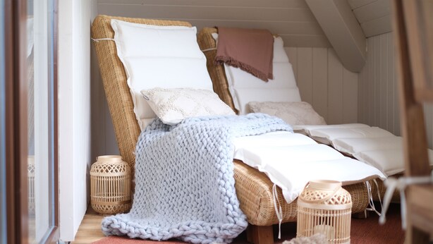 Un dormitorio acogedor con una cama de mimbre, almohadas blancas, una manta tejida y dos lámparas de mimbre.