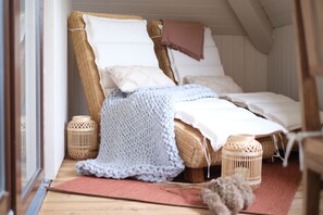 A cozy bedroom with a wicker bed, white pillows, a knitted blanket, and two wicker lamps.