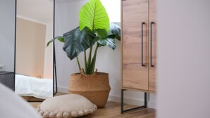 Un dormitorio con una cama, una planta grande en maceta, un armario de madera y un cojín redondo en el suelo.