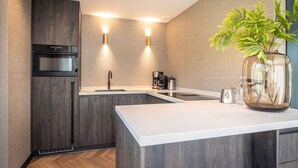 Een moderne keuken met donkerhouten kasten, een roestvrijstalen oven, een dubbele spoelbak en een vaas met groene bladeren op het aanrecht.