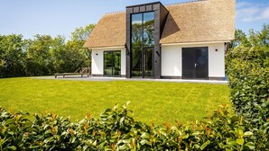 Een modern gebouw met rieten dak, grote glasramen en een verzorgd gazon.