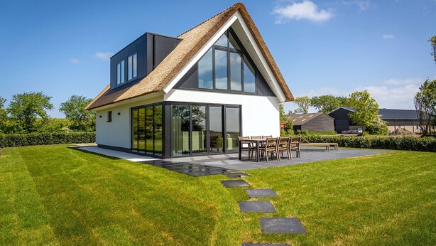 Een modern huis met rieten dak, grote ramen en een verzorgd gazon.