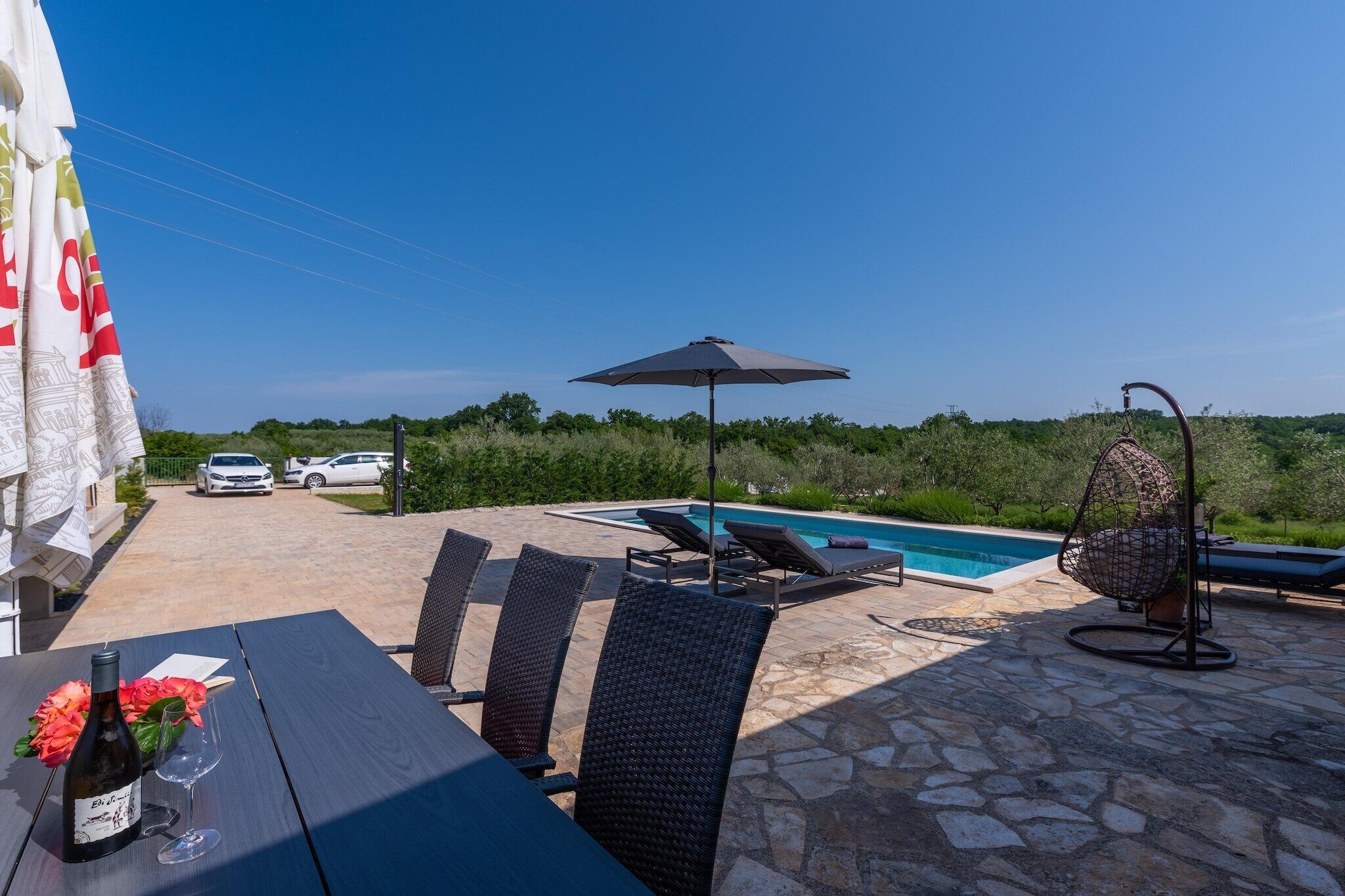 An outdoor patio with a pool, lounge chairs, and a table with a bottle of wine and glasses.