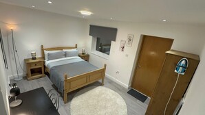 Um quarto com cama de madeira, mesas de cabeceira, mesa de apoio, escrivaninha, cadeira, guarda-roupa, janela e porta.
