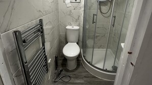 Casa de banho com sanita, cabine de duche e suporte para toalhas.