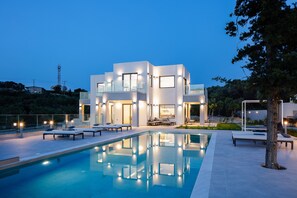 A modern house with a swimming pool, outdoor seating, and a well-lit facade.