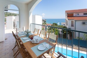 A dining area with a table set for four, overlooking a swimming pool and the sea.