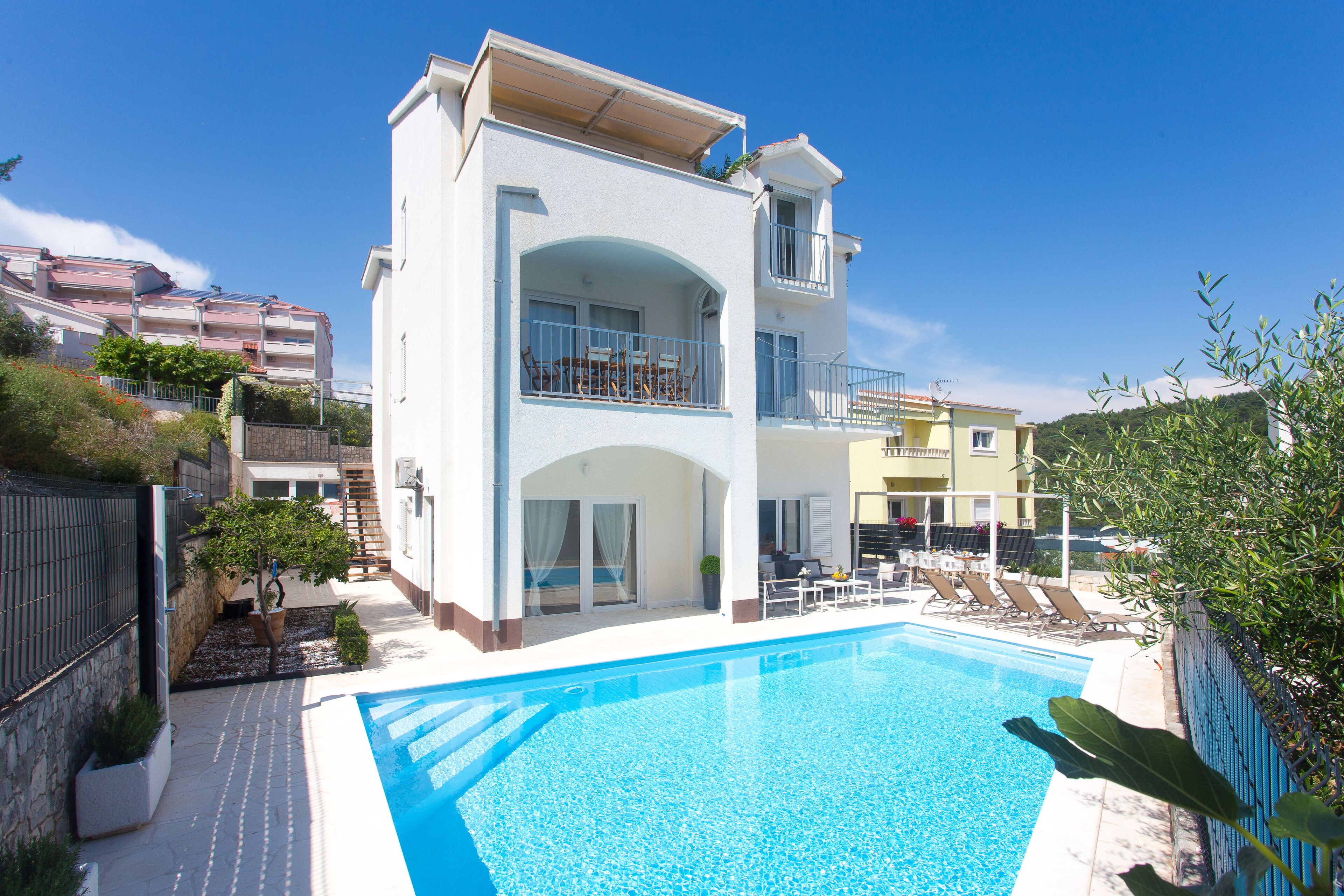 Un edificio a due piani con piscina, area salotto esterna e un balcone.