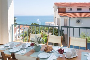 A dining table set with plates, cups, and a vase of flowers, overlooking a coastal view.