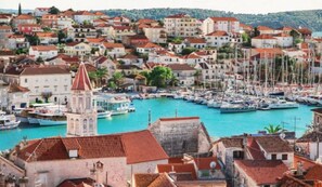 A coastal town with a marina filled with boats, historic buildings with red-tiled roofs, and a prominent tower.