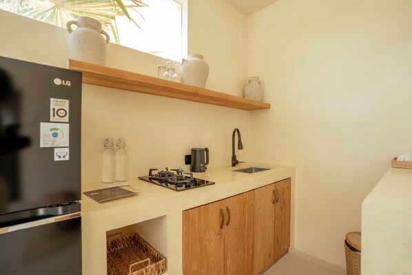 Une cuisine compacte équipée d’un réfrigérateur, d’une cuisinière, d’un évier, de meubles de rangement en bois et d’une étagère où sont disposés des objets décoratifs.