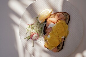 Un sandwich au saumon fumé et à l’œuf, accompagné d’une portion de radis et de laitue râpée, le tout servi sur une assiette en papier.