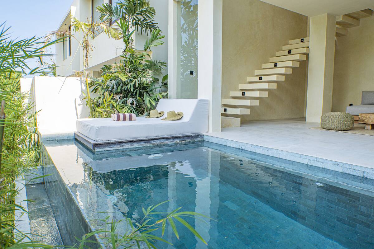 Uma área de piscina moderna com uma piscina infinita branca, um sofá branco com chapéus e uma escadaria com degraus suspensos.