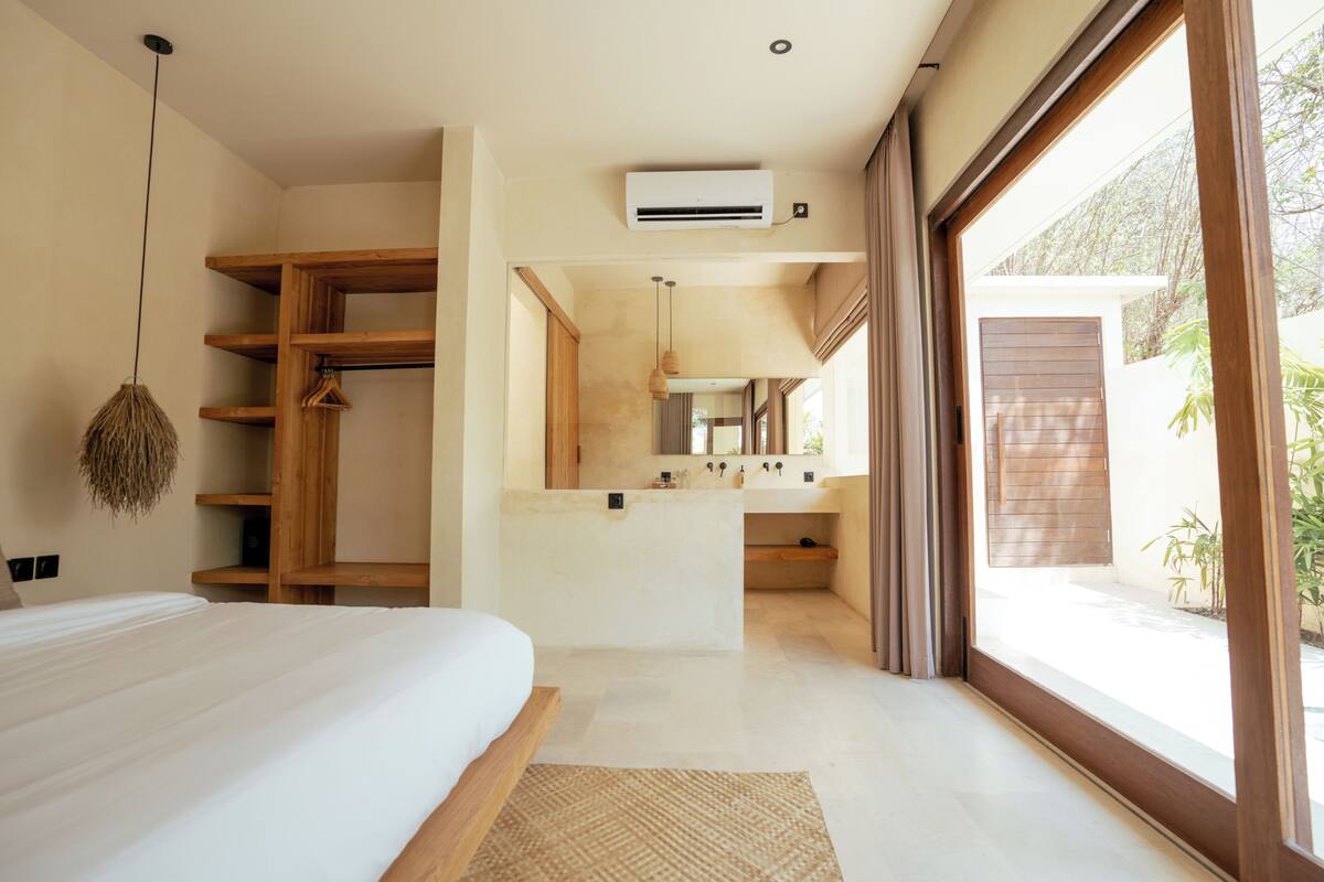 Quarto moderno com cama grande, estantes de madeira, luminária pendente e vista para o exterior.
