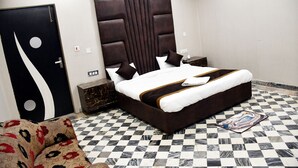 A hotel room with a checkered floor, a large bed with a dark headboard, a floral sofa, and a door with a unique design. - Hotel Aalishan Garden (Bareilly)