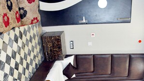 A modern bedroom with a checkered floor, a large bed with a headboard, a wall-mounted TV, and a marble-patterned side table. - Hotel Aalishan Garden (Bareilly)