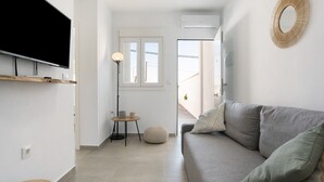 Een moderne woonkamer met een grijze bank, een flatscreen-televisie aan de muur, een ronde spiegel en een kleine ronde tafel met een lamp.