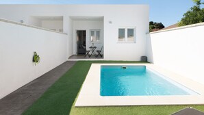 Een modern huis met een zwembad, een terras met een tafel en stoelen, en een kleine tuin.