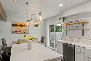 Une cuisine moderne avec des meubles blancs, un lave-vaisselle et un coin repas comprenant une table et des chaises.