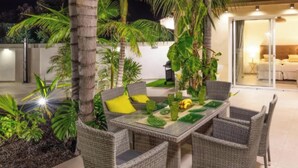Eine Terrassenausstattung mit Korbmöbeln, einem Esstisch und tropischen Pflanzen.