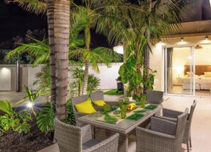 Une terrasse extérieure aménagée avec des meubles en osier, une table à manger et des plantes tropicales.