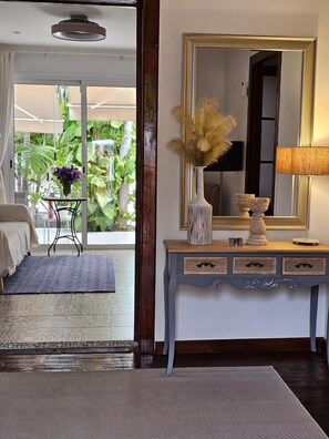 A room with a bed, a console table with a mirror, a vase with dried plants, and a view of greenery outside.