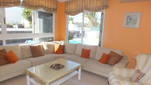 A living room with a beige sofa, a striped armchair, a coffee table, and a pool view.
