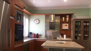 A kitchen with stainless steel appliances, wooden cabinets, a clock, and a coffee maker.