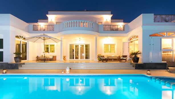 A modern house with a swimming pool, outdoor seating, and a well-lit entrance.